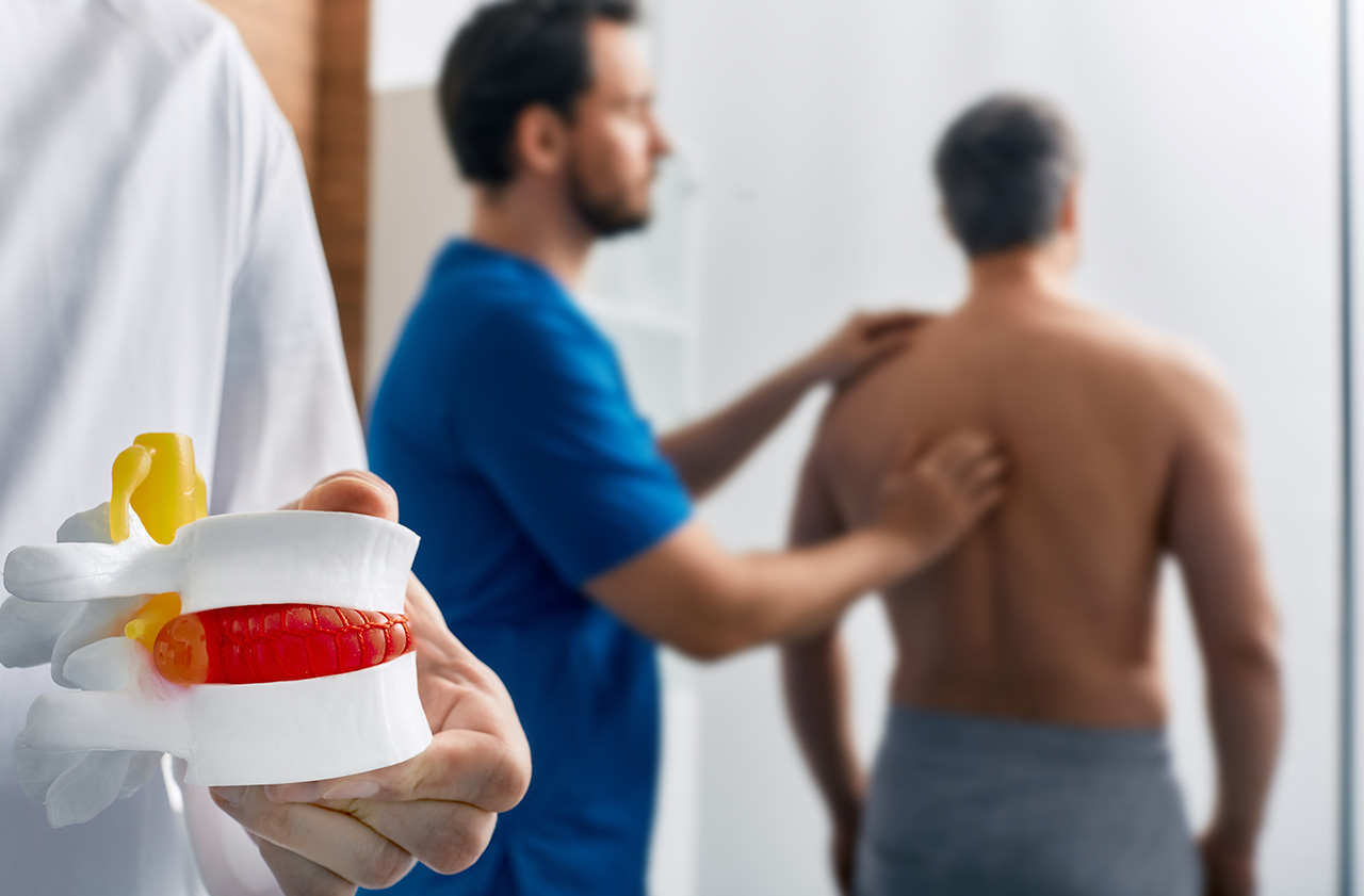Doctor holding a spine model while explaining herniated discs.